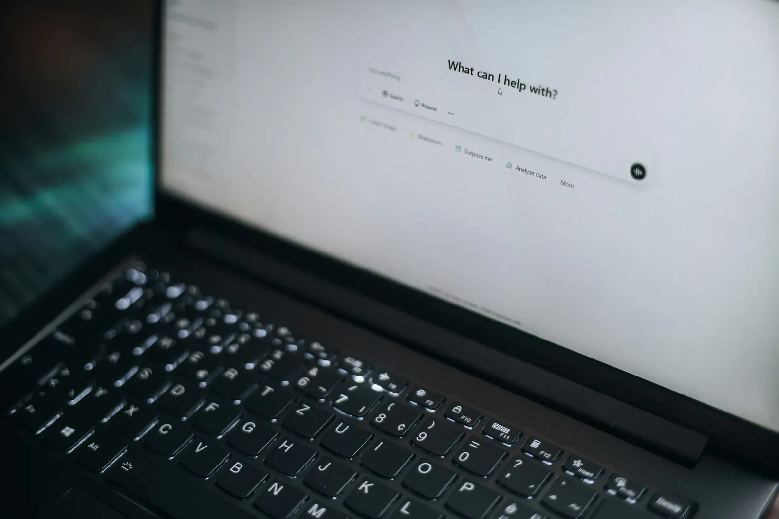 Close-up of a laptop keyboard and screen showing an AI assistant prompt box that asks what it can help with
