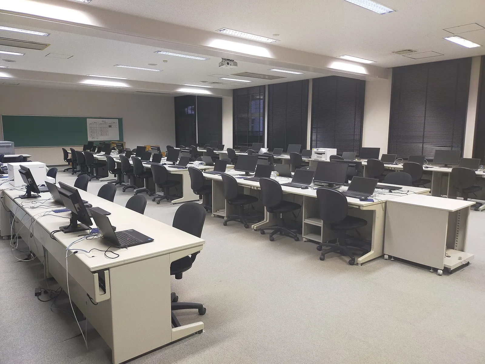 Empty computer classroom with rows of desks, laptops, office chairs and a whiteboard at the front