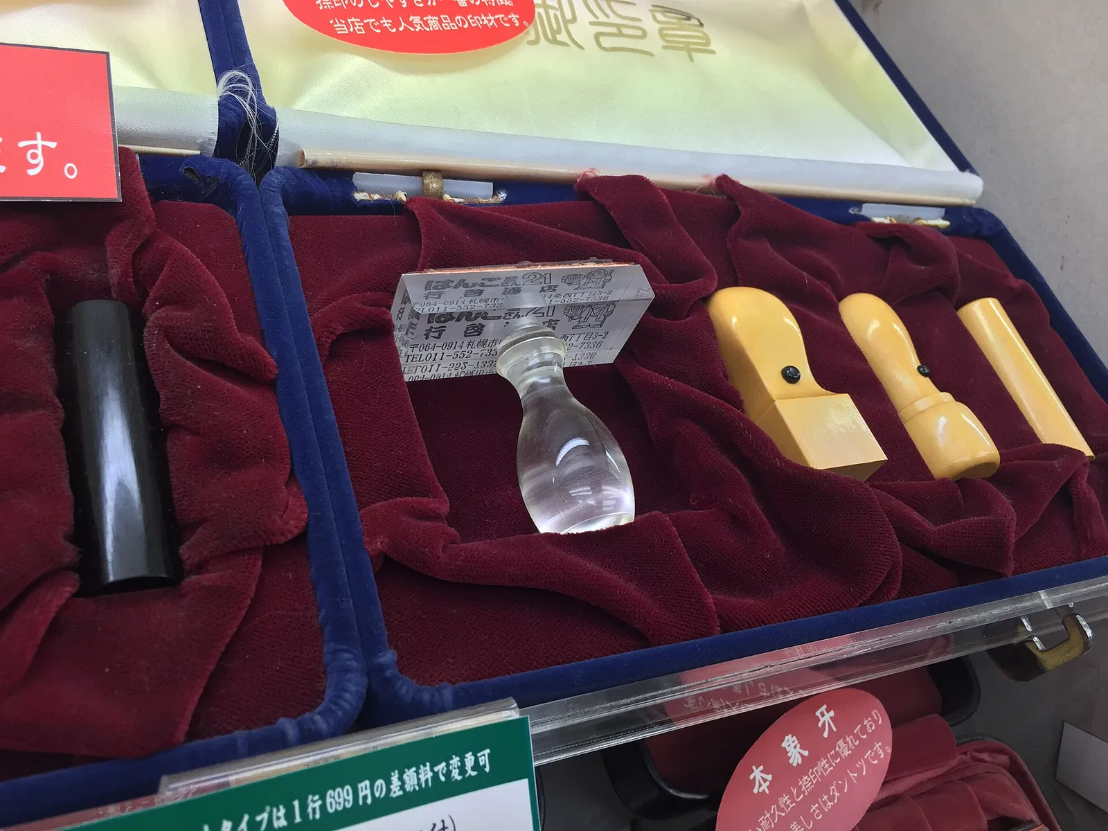 Display case of Japanese hanko seals on red velvet, with black, clear acrylic and yellow stamp handles