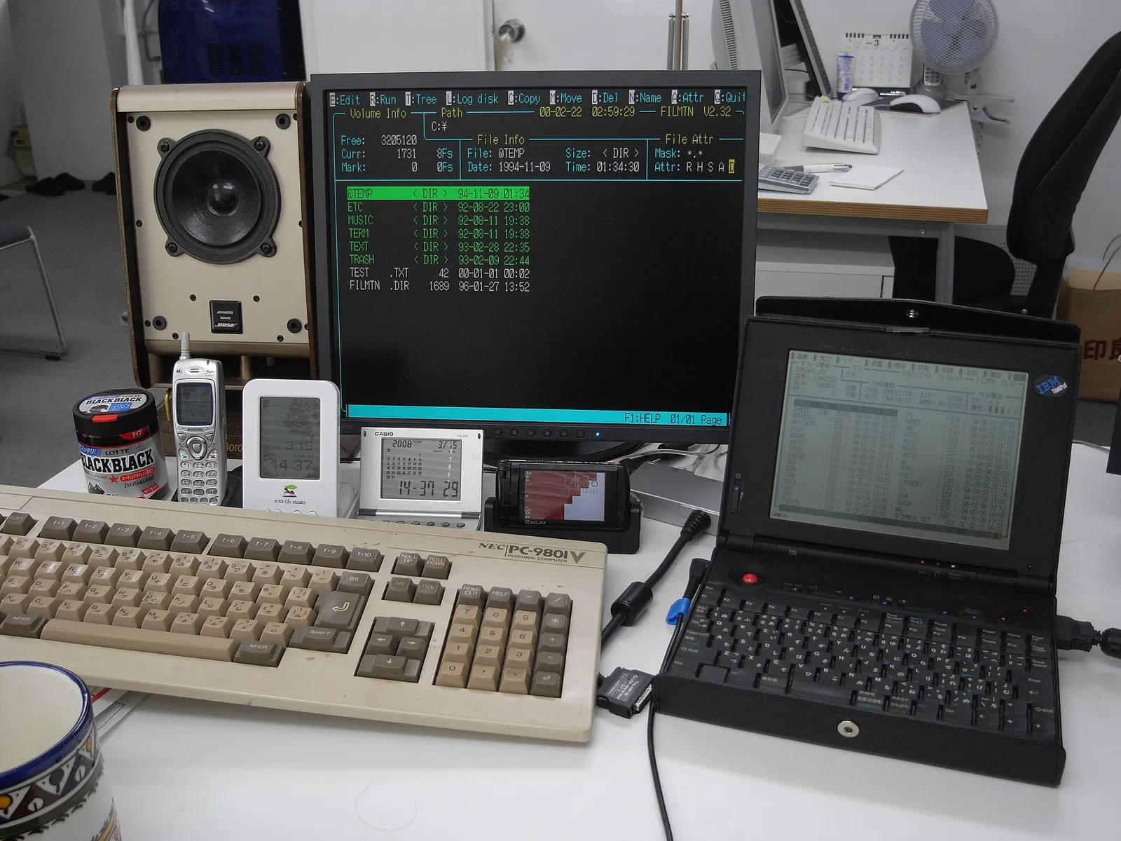 An NEC PC-9801 keyboard and monitor on a desk beside a small IBM ThinkPad 220 laptop connected by cable