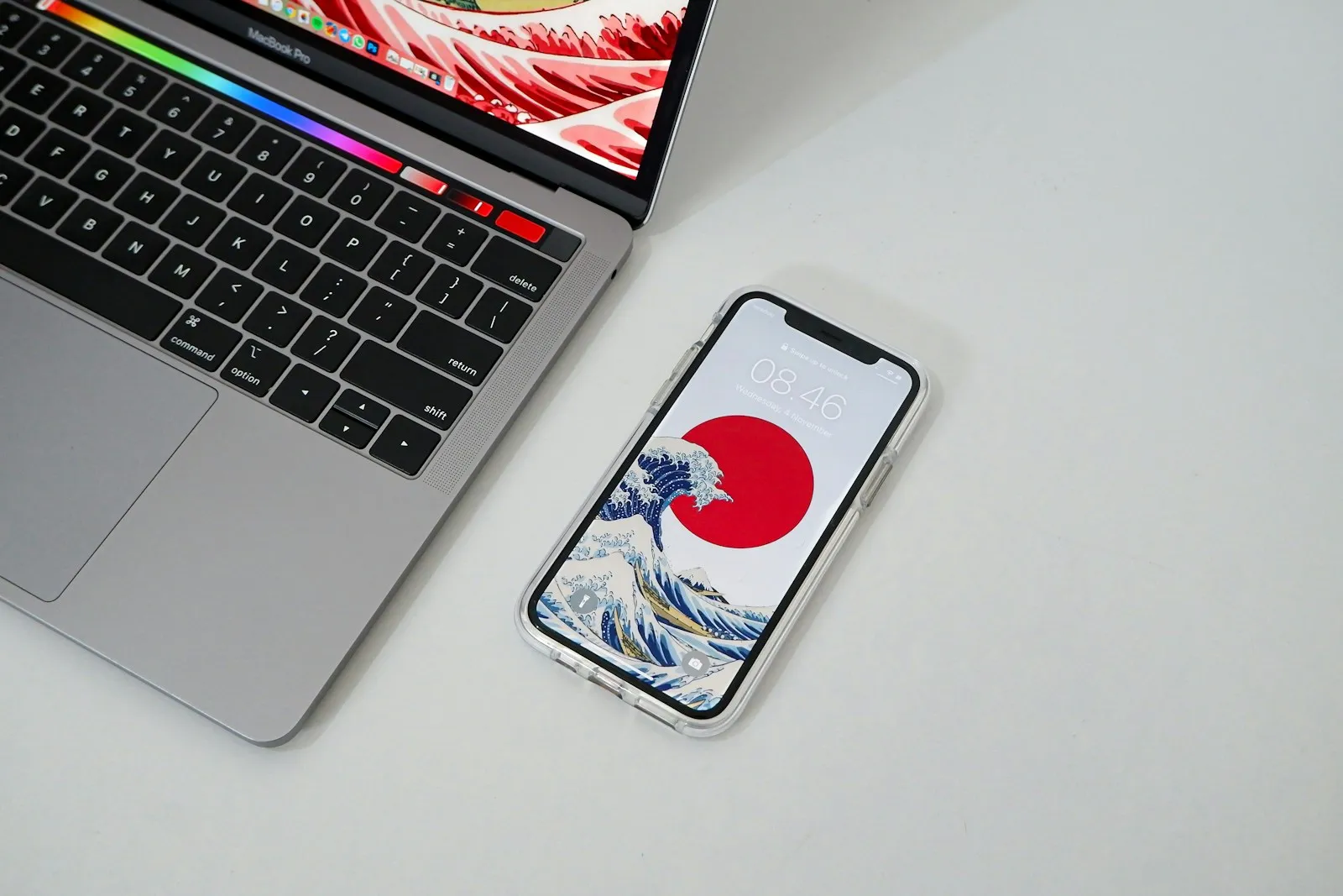 A MacBook Pro and an iPhone showing a Great Wave wallpaper side by side on a white desk