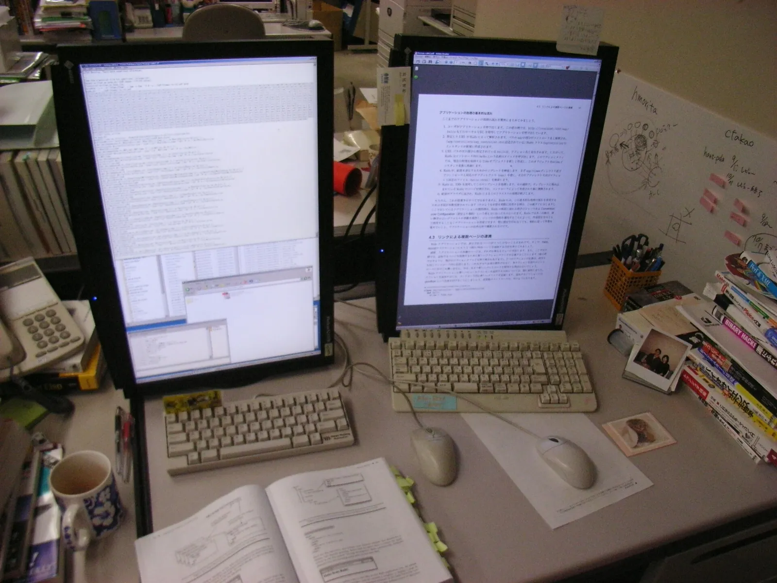 Office desk with two portrait monitors, two beige keyboards, a desk phone, stacked books and a coffee mug