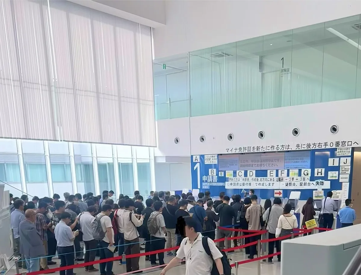 A long queue of people standing behind red rope barriers in the bright, modern lobby of the Kanagawa driver's licence centre