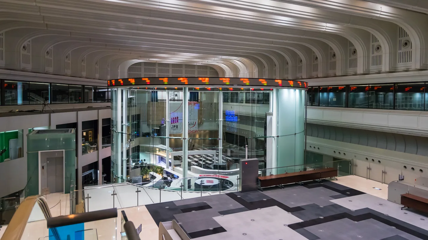 The main hall of the Tokyo Stock Exchange in Kabutocho, with a glass cylinder at its center ringed by a scrolling red stock ticker under an arched white ceiling