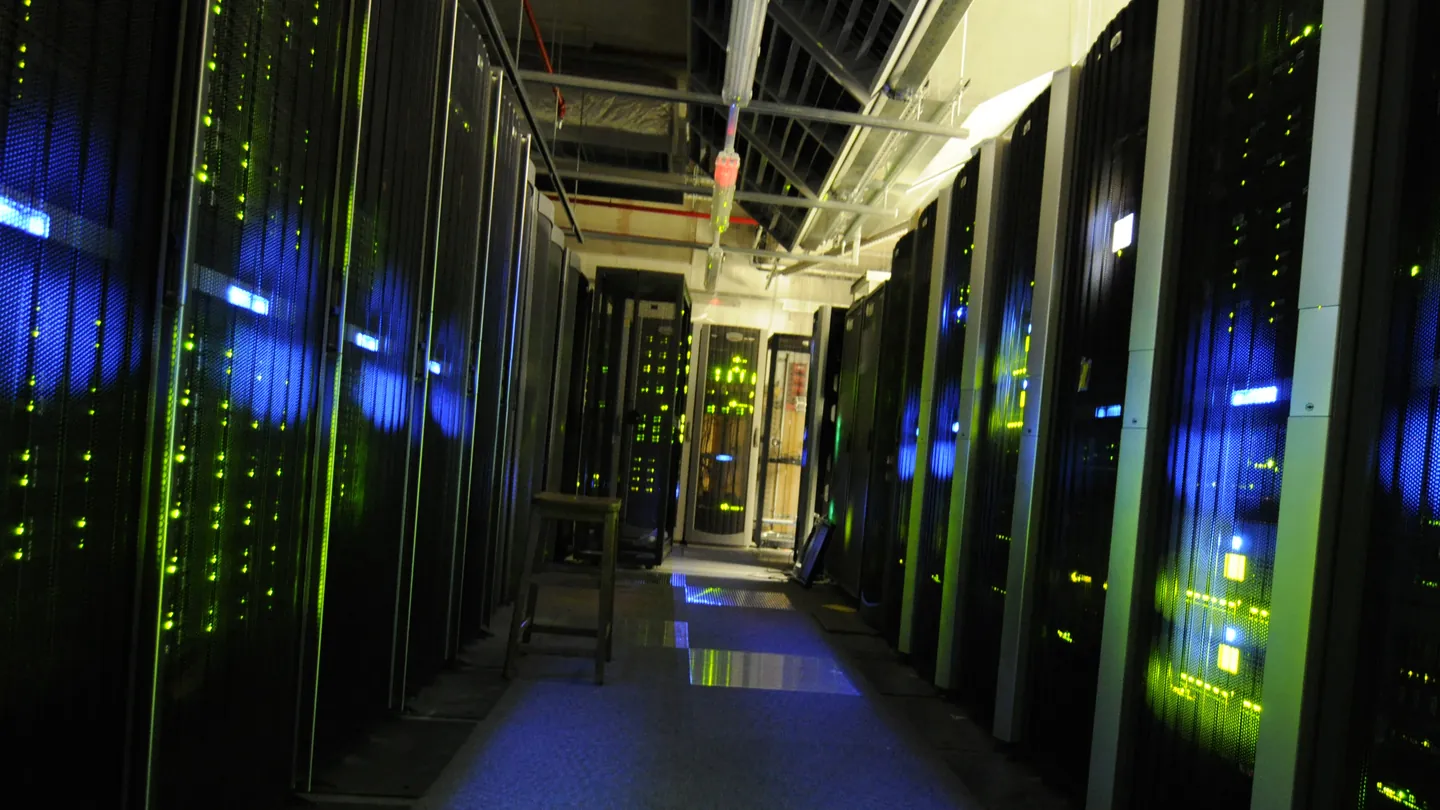 A dim corridor between rows of server racks lit by green and blue status lights