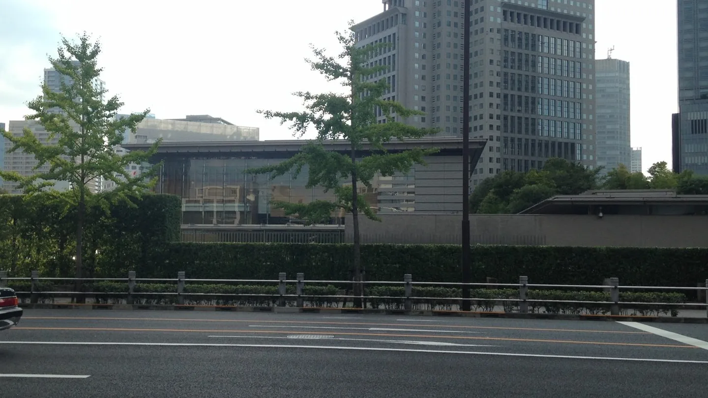 The low glass-and-stone Prime Minister's Office in Tokyo behind a hedge and young ginkgo trees, with office towers rising behind it