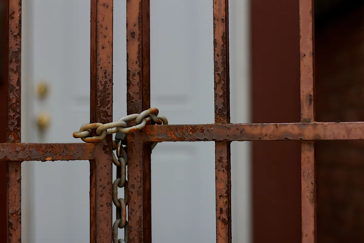 A rusted iron gate chained shut in front of a closed white door