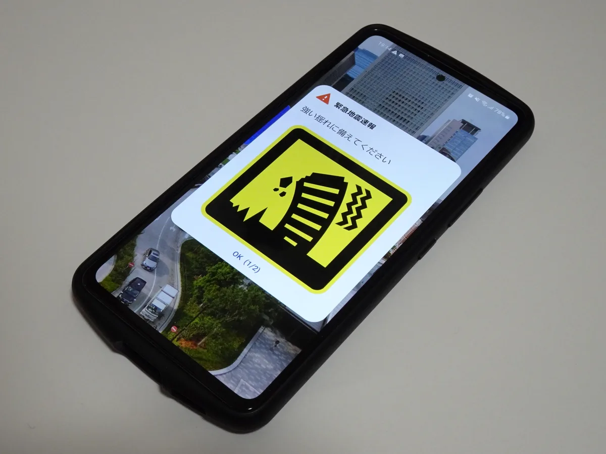 A smartphone lying on a table showing a Japanese Earthquake Early Warning screen with a yellow shaking-building icon