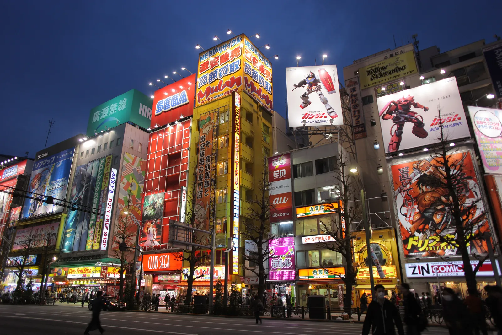 Akihabara main street at dusk with illuminated buildings covered in anime, game and electronics store signs