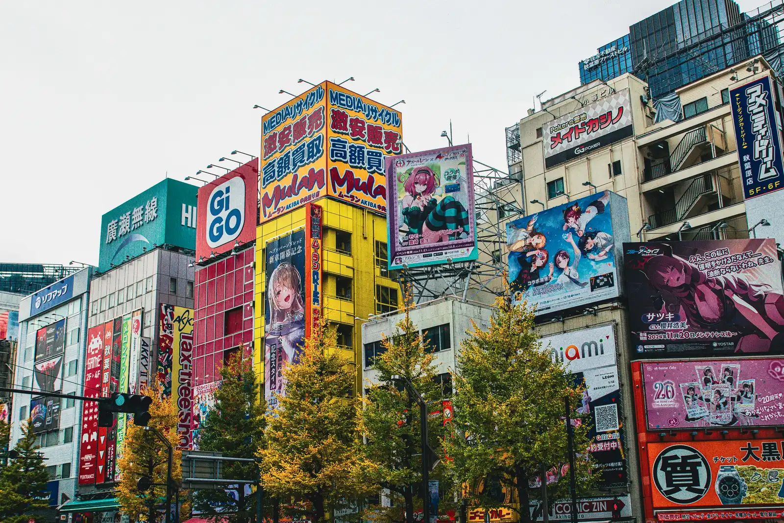 Buildings in Akihabara, Tokyo, covered with large anime and manga advertising billboards above a tree-lined street