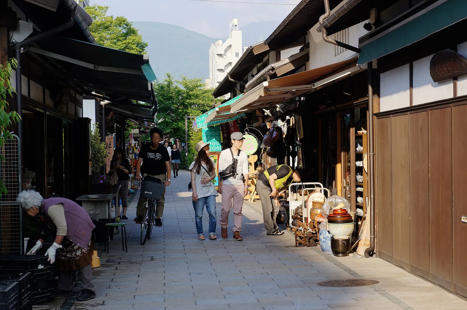 Shoppers and a cyclist on Nawate shopping street in Matsumoto, lined with low wooden shopfronts