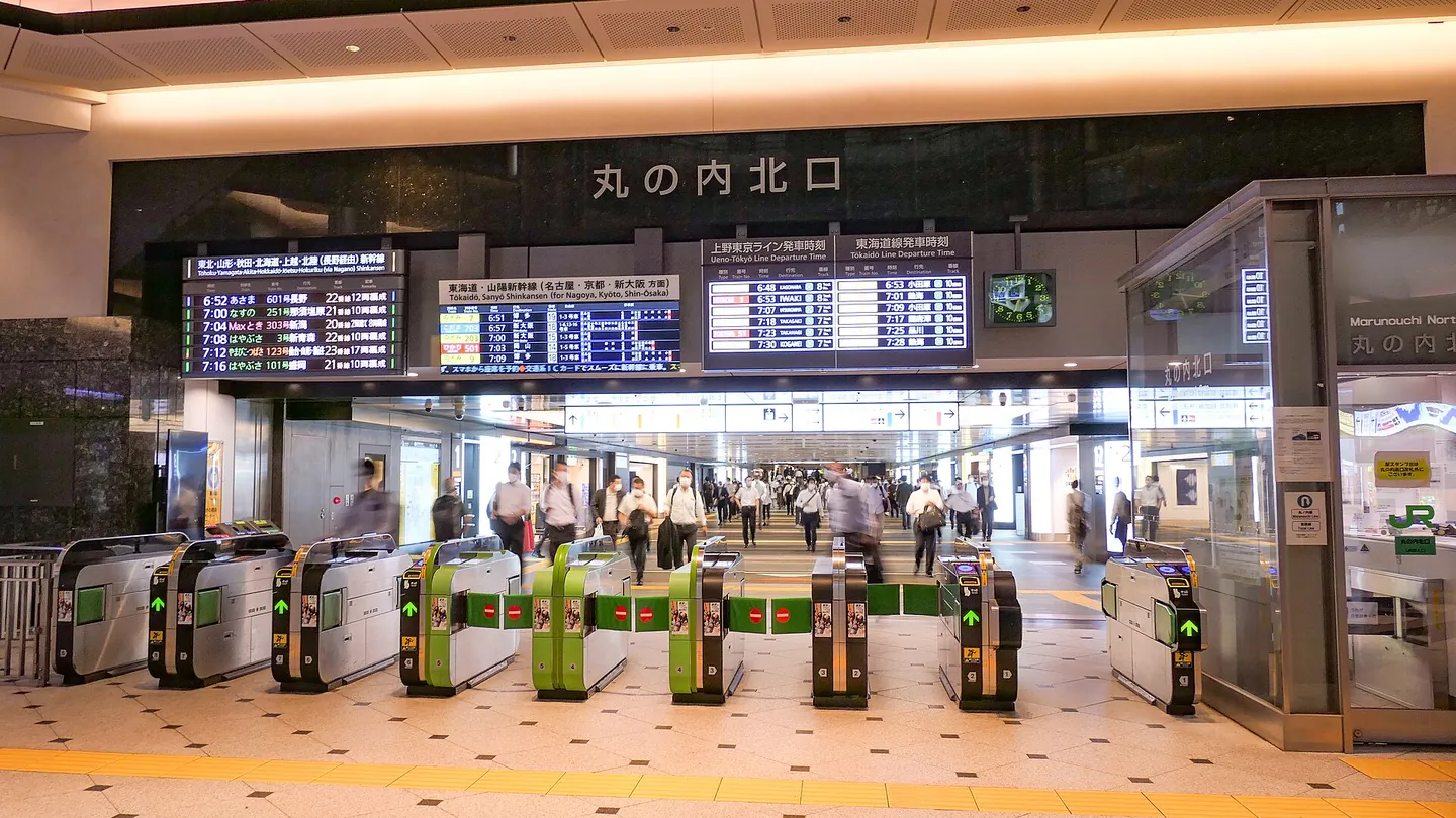 Commuters walking through a row of green and silver JR ticket gates under departure boards and a sign reading 丸の内北口