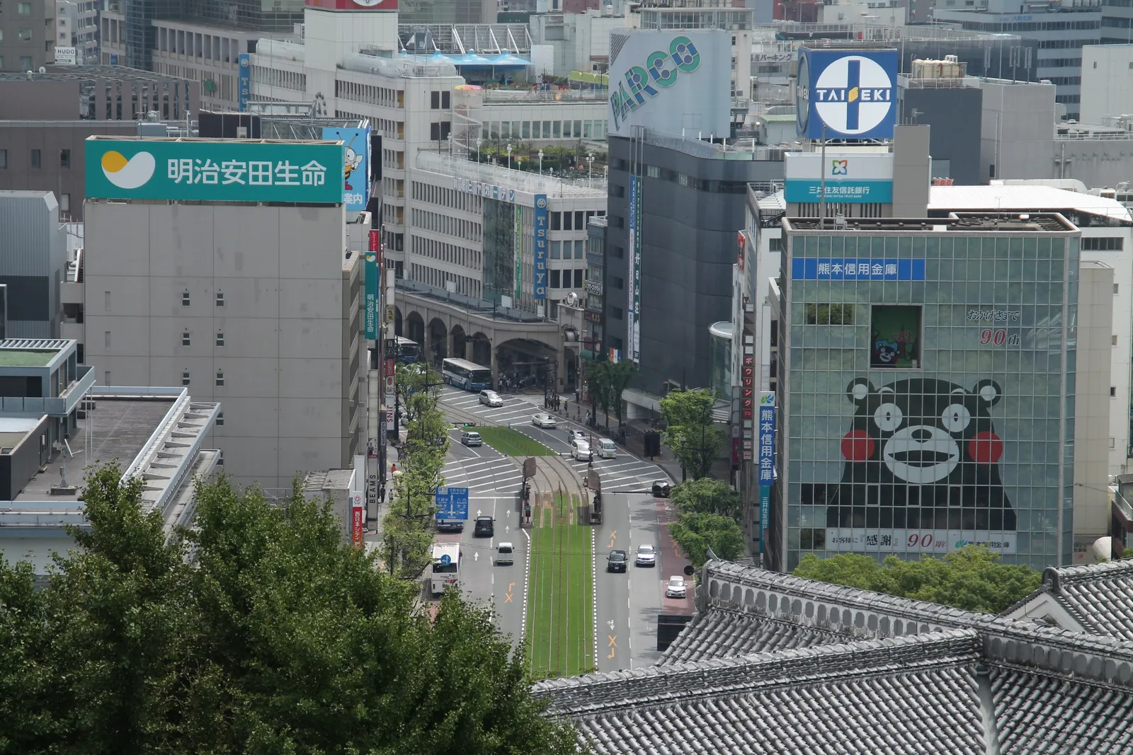 Large Kumamon mascot artwork on the side of an office building above a tram street in central Kumamoto