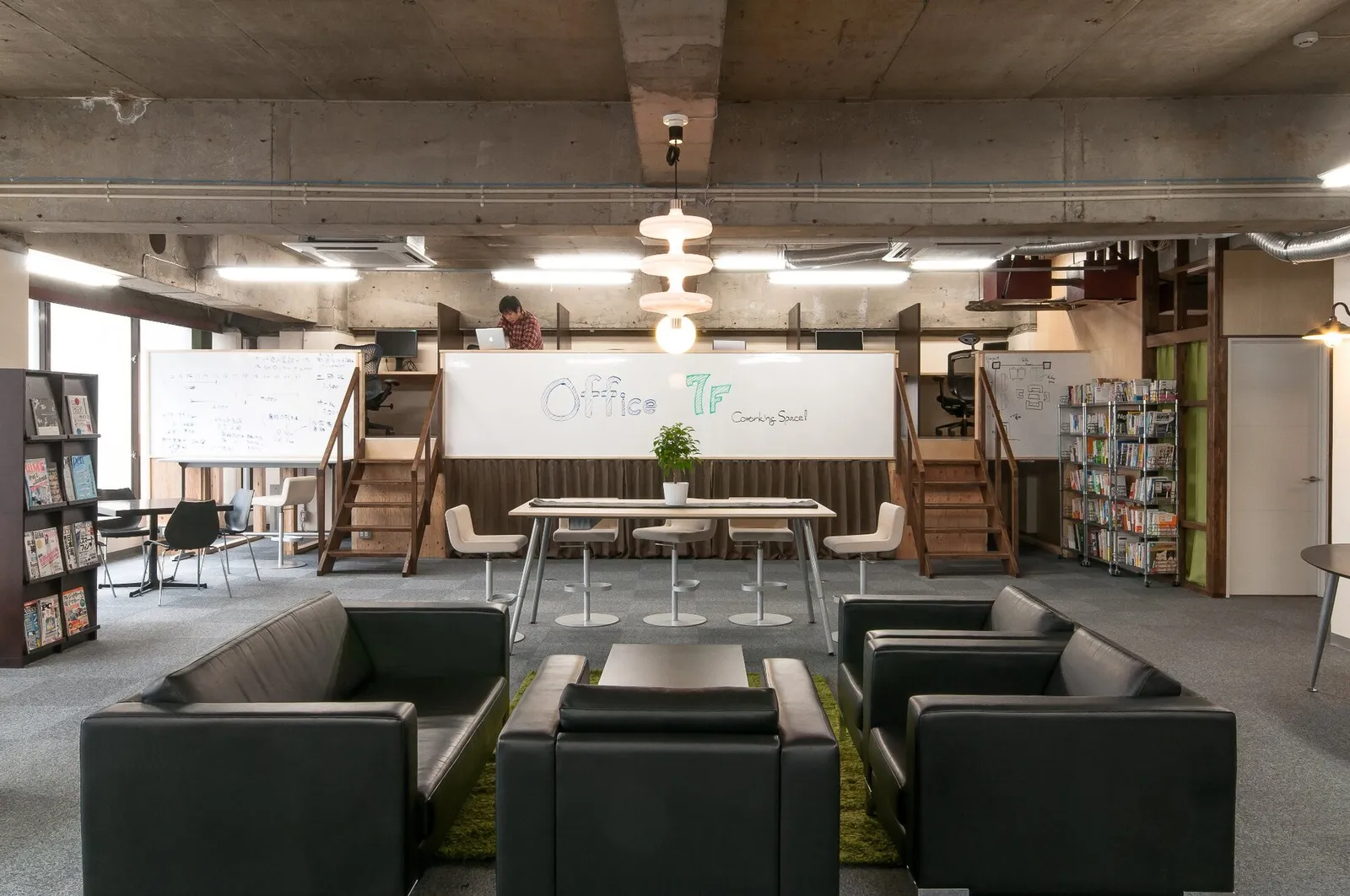 Coworking space with black leather sofas, a long shared table, bookshelves and a wooden mezzanine loft