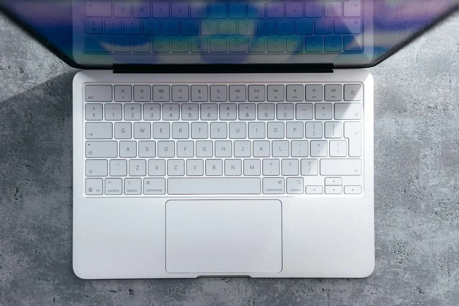 Top-down view of an open silver MacBook keyboard and trackpad on a grey concrete surface