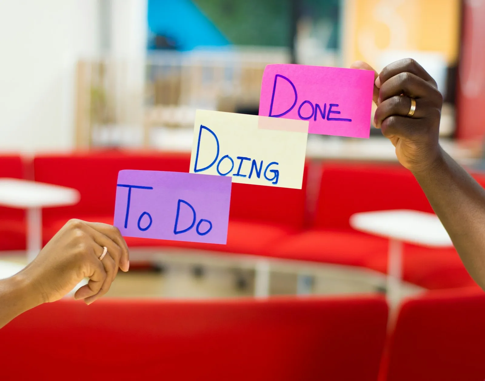 Two hands holding up sticky notes labelled To Do, Doing and Done in an office