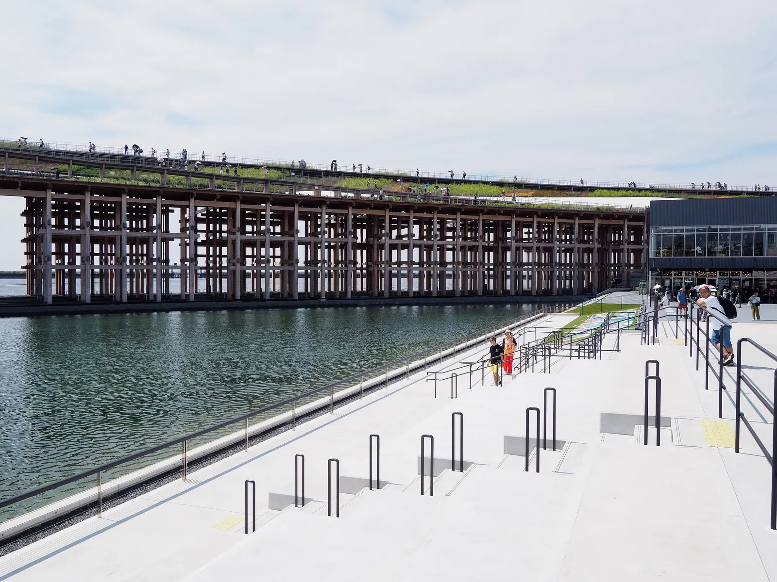 Timber frame of the Grand Ring at Expo 2025, with visitors on its roof walkway above a water terrace