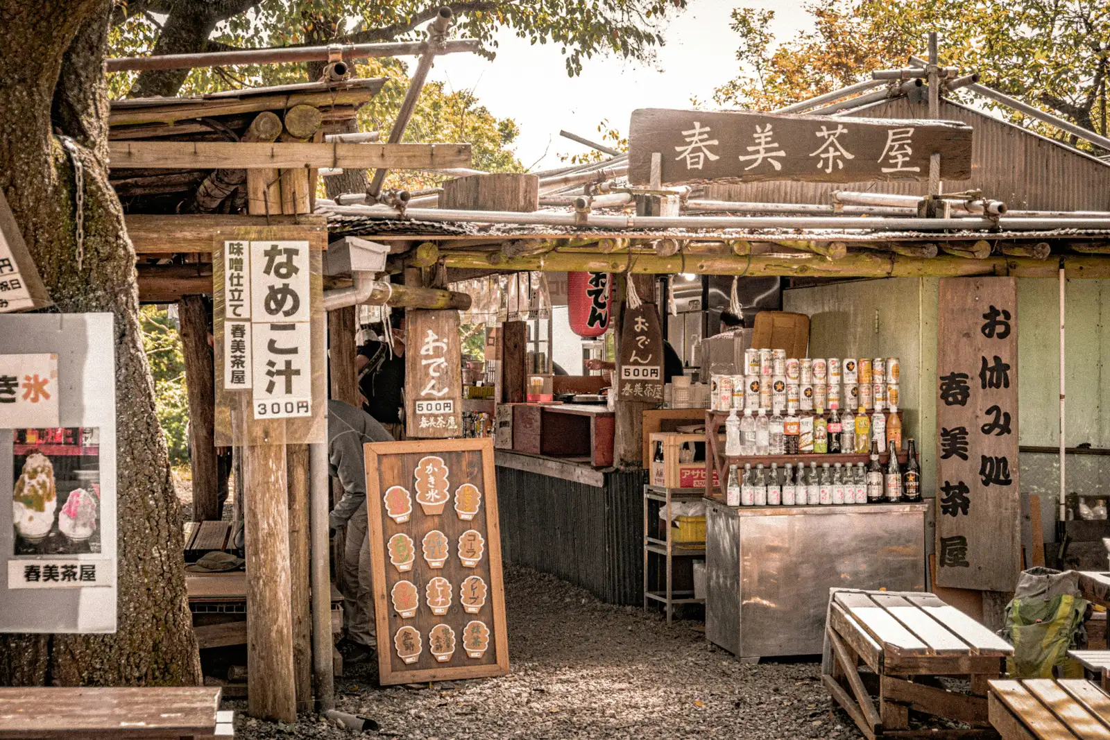 A rustic wooden tea stall with handwritten signs and bottles on its shelves in a mountain area of Japan