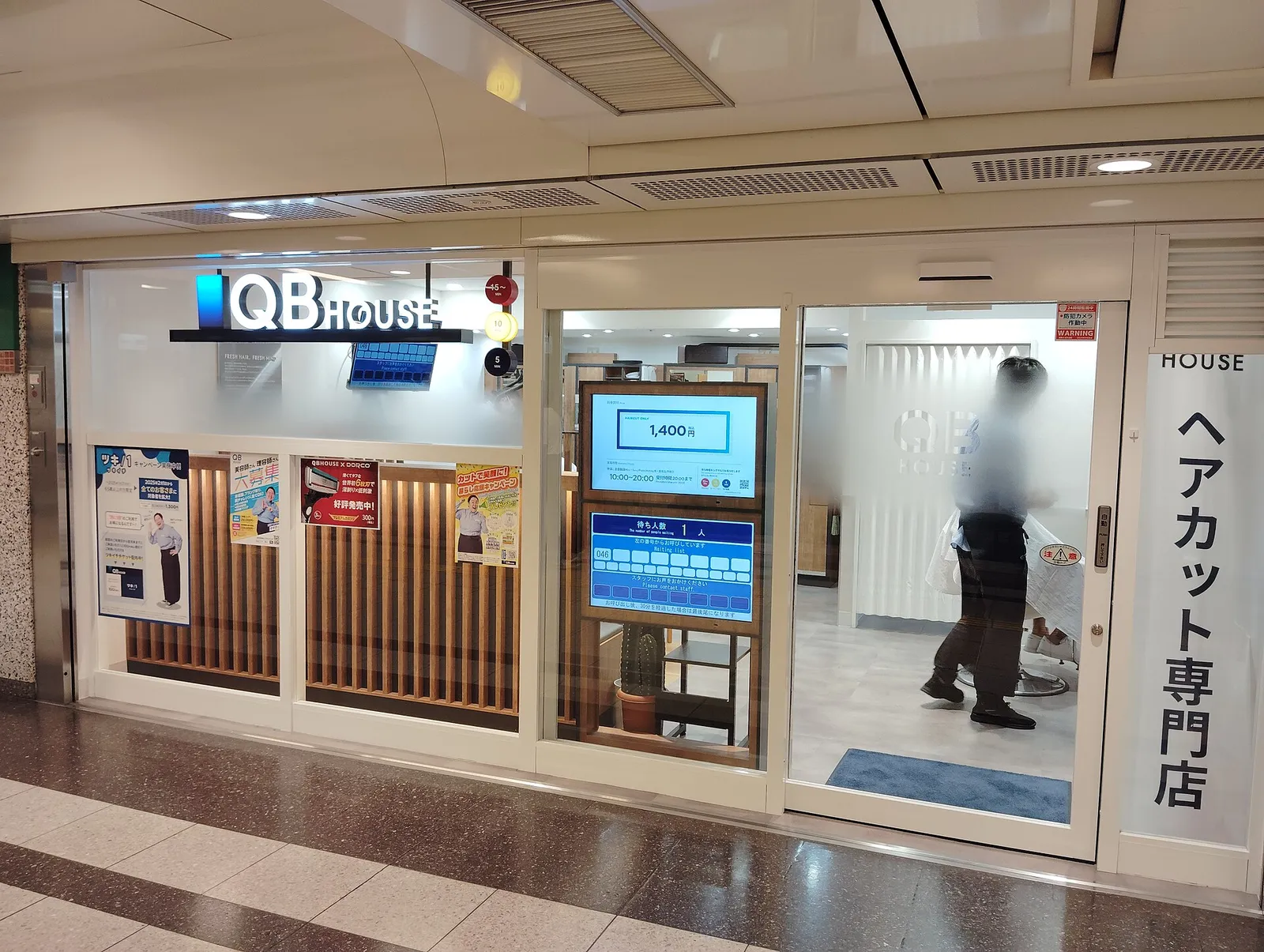 Storefront of a QB House haircut shop in an underground mall, with its fixed price shown on a screen