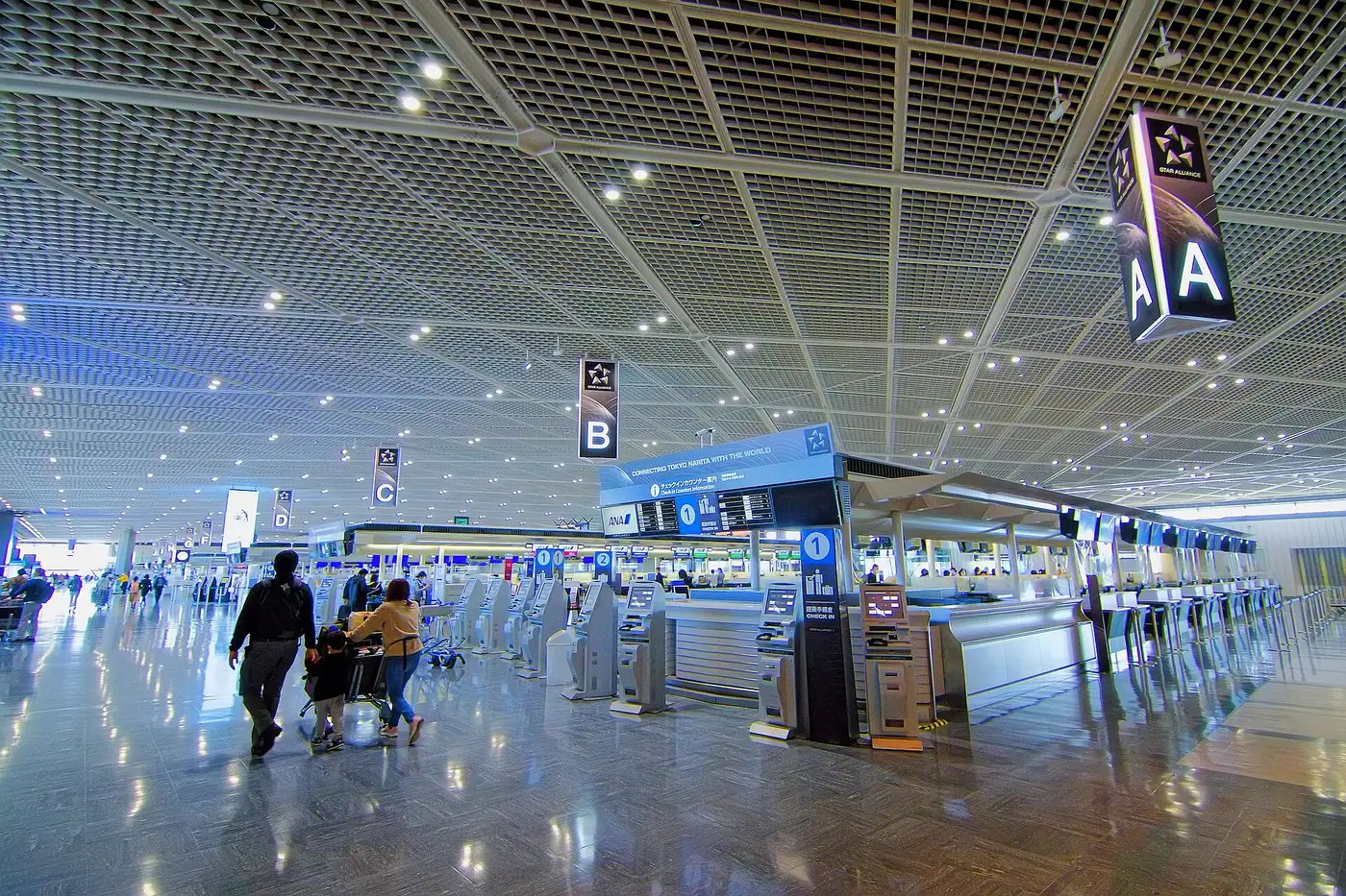 Travelers with luggage walking through the bright departure lobby of Narita Airport Terminal 1 South Wing