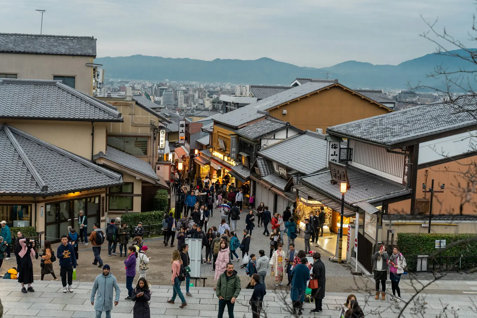 Crowds of visitors walking down a sloping stone street lined with traditional wooden shops in Higashiyama, Kyoto