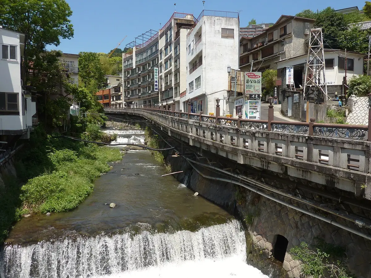 The Fujiki River running through Yugawara Onsen past a small weir, a stone embankment and hotel buildings