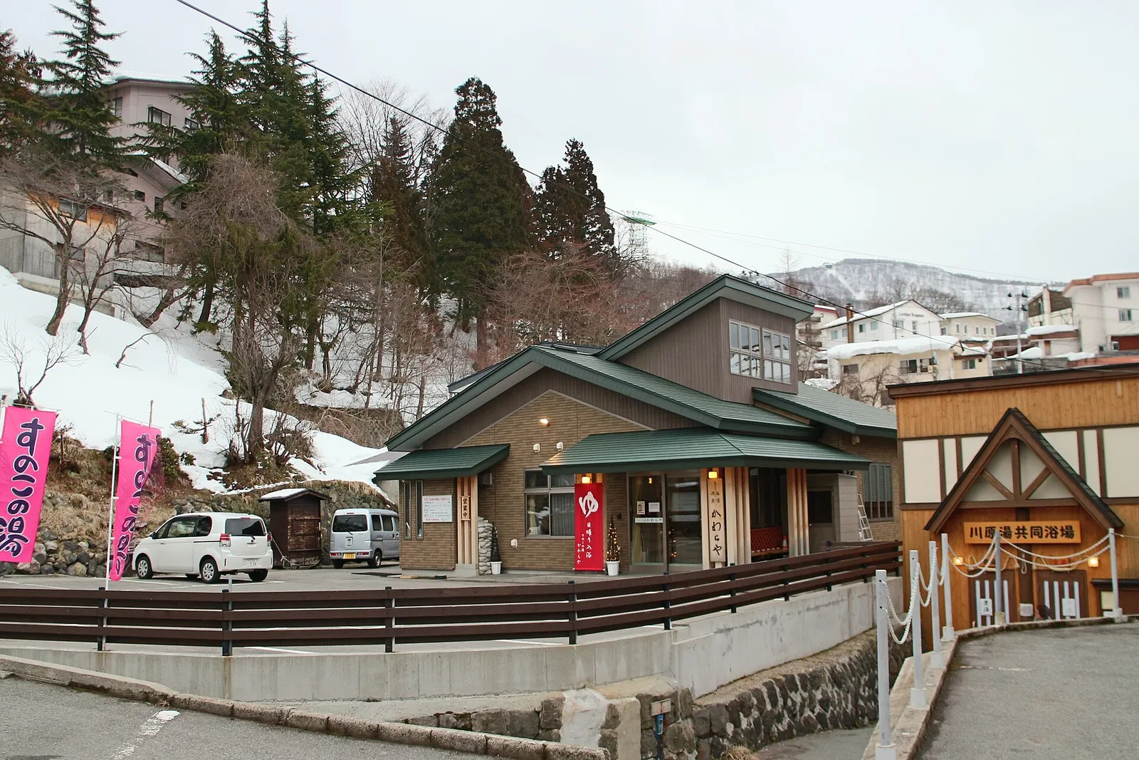 Wooden buildings and a parking area beside snowbanks in the hot spring town of Zaō Onsen, Yamagata