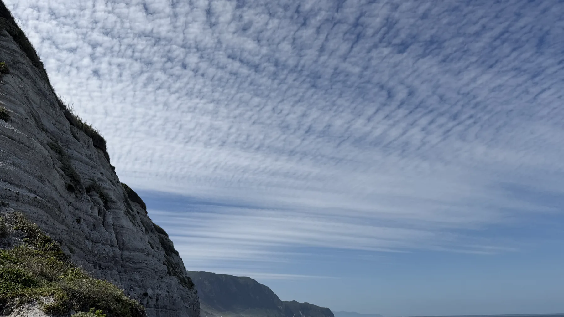 Coastal cliff in Japan under a wide patterned sky with the horizon in the distance