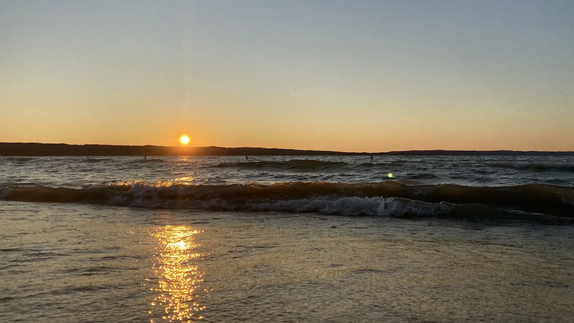 The sun low over the sea, with small waves breaking and its light reflected on the wet shore